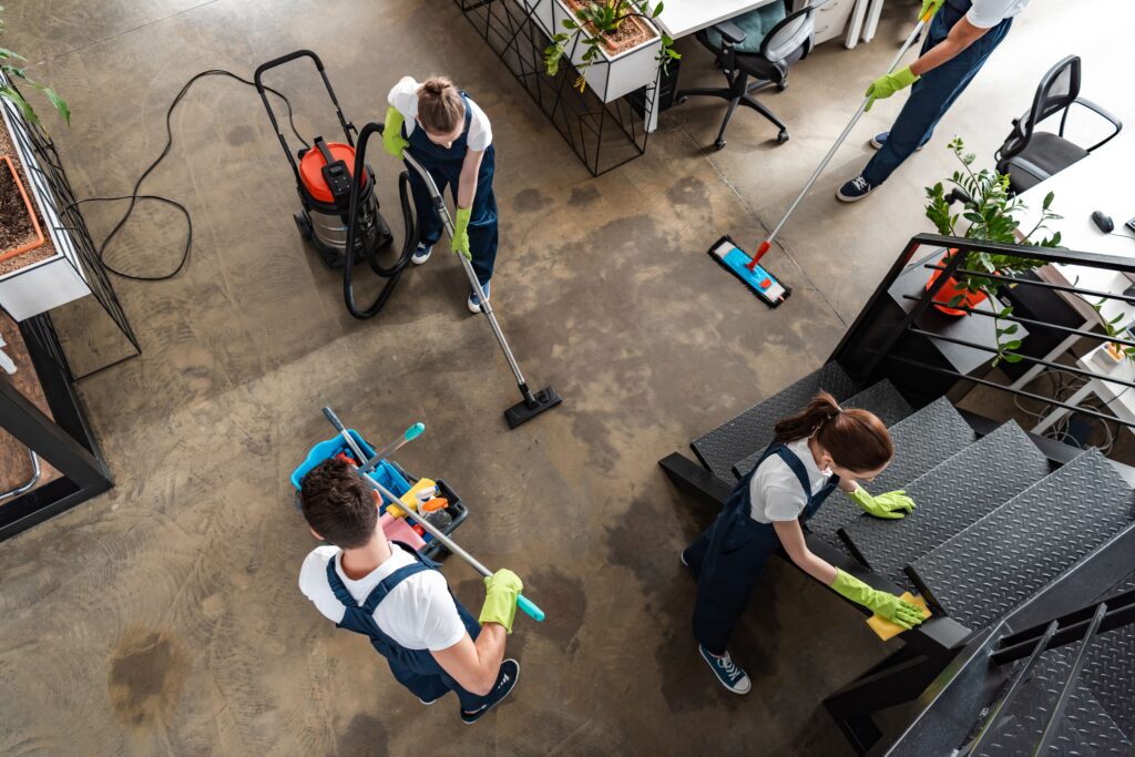 A commercial property being cleaned by the best cleaning service company in Qatar. One moping the floor, another employee vaccuuming and another employee dusting the stairs.